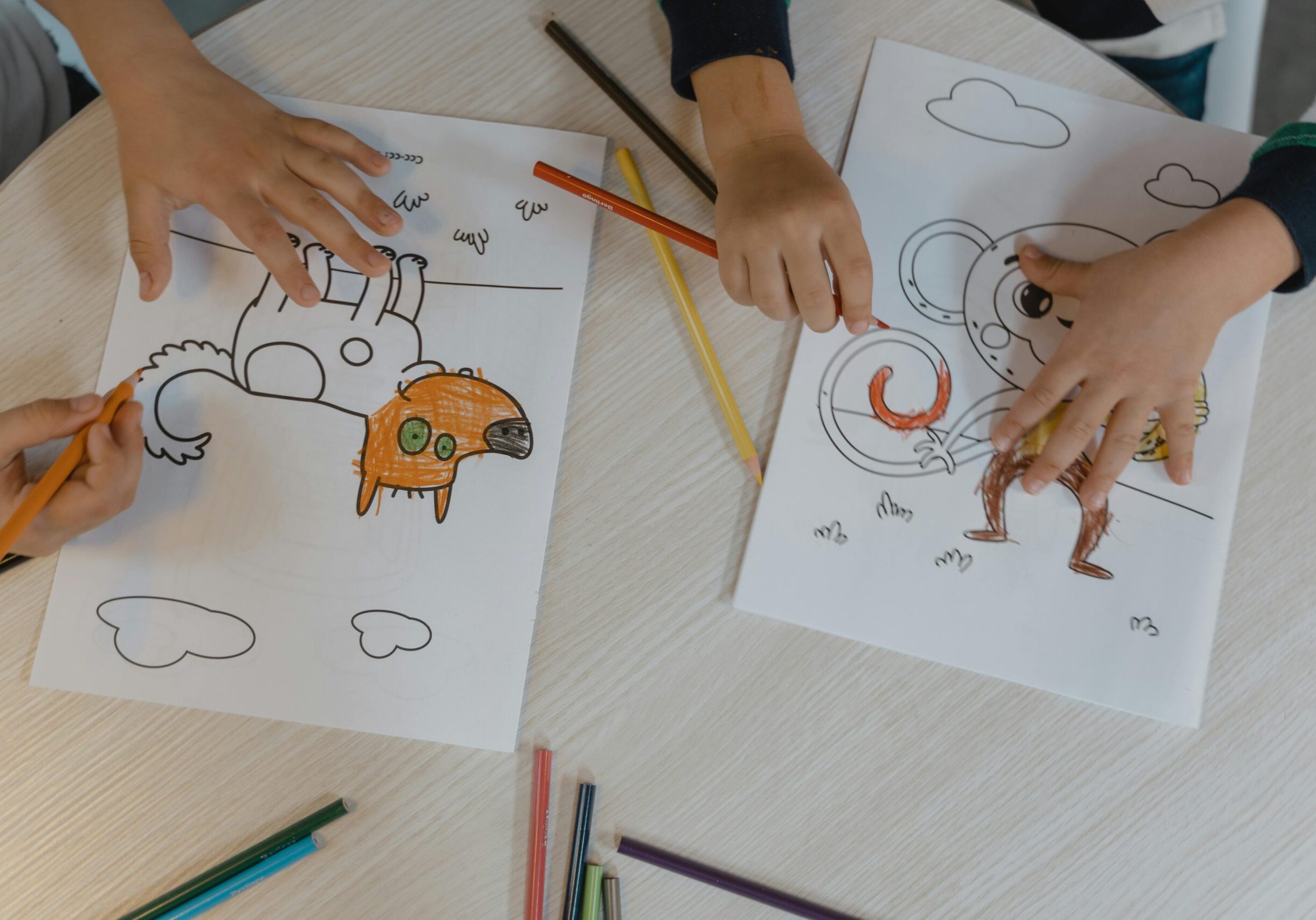 Children using colored pencils to bring animal drawings to life on a wooden table.